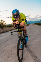 Image showing Triathlete riding his bicycle during sunset, preparing for a marathon. The warm colors of the sky provide a beautiful backdrop for his determined and focused effort.