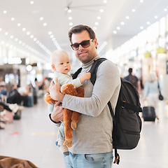 Image showing Father traveling with child, holding his infant baby boy at airport terminal waiting to board a plane. Travel with kids concept.