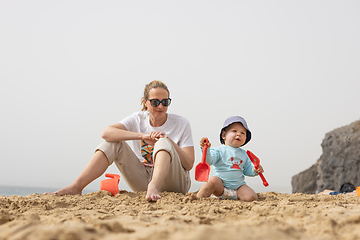 Image showing Mother playing his infant baby boy son on sandy beach enjoying summer vacationson on Lanzarote island, Spain. Family travel and vacations concept.