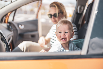 Image showing Mother and her infant baby boy child on family summer travel road trip, sitting at dad's front seat, waiting in the car for father to buy farry tickets.