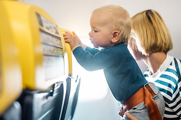 Image showing Mother and infant baby boy child flying on comercial flight, traveling by plane, sitting together at window seat. Flying with kids.