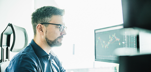 Image showing Stock broker trading online watching charts and data analyses on multiple computer screens.