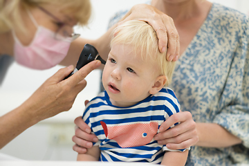 Image showing Infant baby boy child being examined by his pediatrician doctor during a standard medical checkup in presence and comfort of his mother. National public health and childs care care koncept.