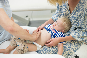 Image showing Infant baby boy child being examined by his pediatrician doctor during a standard medical checkup in presence and comfort of his mother. National public health and childs care care koncept.