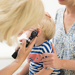 Image showing Infant baby boy child being examined by his pediatrician doctor during a standard medical checkup in presence and comfort of his mother. National public health and childs care care koncept.