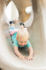 Image showing Child playing on outdoor playground. Toddler plays on school or kindergarten yard. Active kid on stone sculpured slide. Healthy summer activity for children. Little boy climbing outdoors.