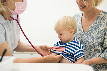 Image showing Infant baby boy child being examined by his pediatrician doctor during a standard medical checkup in presence and comfort of his mother. National public health and childs care care koncept.