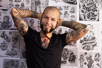 Image showing Tattoos, creativity and portrait of a male artist standing by sketches or drawings in his studio. Happy, smile and face of a punk man with a edgy, funky and body art or ink creative business store.