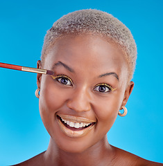 Image showing Portrait, makeup and eyeshadow with a black woman on a blue background in studio to apply a beauty product. Face, gold color on a brush and a happy young female model posing for style or glamour