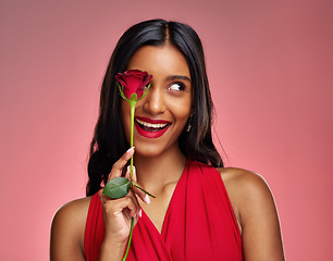 Image showing Excited, beauty and face of a woman with a rose on a studio background for valentines day. Makeup, model and happy young Indian girl with a flower in hand for romance or love on pink backdrop