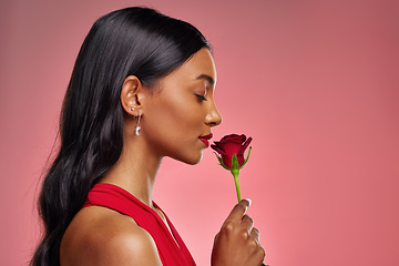 Image showing Face, woman and smelling a rose on a studio background for valentines day. Fragrance, model and profile of a young Indian girl with a flower in hand for romance, scent or love on pink backdrop