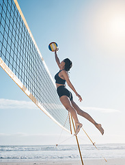 Image showing Woman, jump and volleyball in air on beach by net in serious sports match, game or competition. Fit, active and sporty female person jumping or reaching for ball in volley or spike by the ocean coast