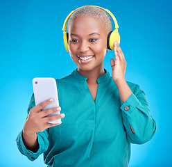 Image showing Headphones, phone and woman listening on studio, blue background for podcast, music and streaming service. Mobile, audio technology and young african woman on electronics for radio, sound or hearing