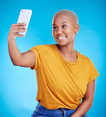 Image showing Phone, selfie and smile with a black woman on a blue background in studio to update her status. Mobile, social media and a happy young female influencer taking a photograph for online profile