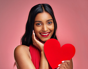 Image showing Portrait, heart and romance with a woman on a pink background in studio for love or affection. Smile, emoji and social media with a happy young female holding a shape or symbol on valentines day