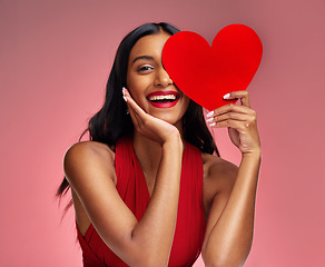 Image showing Woman, paper heart and smile in studio portrait for makeup, beauty or romantic sign by red background. Happy girl, fashion model or cardboard emoji for love, cosmetic or happy for valentines day date