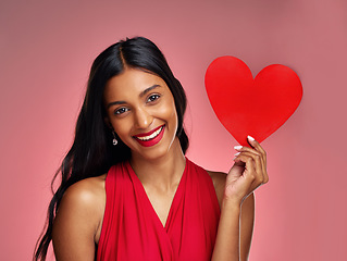 Image showing Portrait, heart and smile with a woman on a pink background in studio for love or romance. Valentines day, emoji and social media with a happy young female holding a shape or symbol of affection