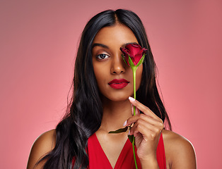 Image showing Face, beauty and portrait of a woman with a rose on a studio background for valentines day. Makeup, model and serious young Indian girl with a flower in hand for romance or love on pink backdrop