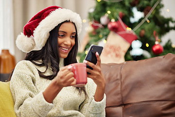 Image showing Christmas, happy woman and phone on home sofa with a smile and coffee for online communication. Indian female person with a smartphone and hot chocolate for festive holiday, social media or internet