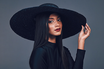 Image showing Face, fashion and serious woman with hat in studio isolated on a gray background. Portrait, style and confident female model from India with makeup cosmetics, classy clothes and elegant aesthetic.