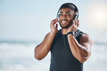 Image showing Music, headphones and happy man at the beach after fitness routine with podcast on mockup space. Radio, wellness and Indian male runner walking along the ocean after sports, training or workout