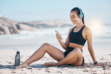 Image showing Fitness, break and happy woman relax at beach with phone, music and headphones after training. Exercise, resting and lady health influencer posting to social media, blog or podcast after ocean run