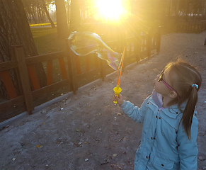 Image showing A little girl blowing soap bubbles in summer park. Background toninf for instagram filter