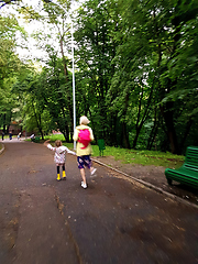 Image showing Mother and little curly toddler girl walking together in a park on a wet summer day after rain, view from the back