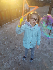 Image showing A little girl blowing soap bubbles in summer park. Background toninf for instagram filter