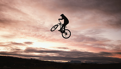 Image showing Sunset, dirt bike and jump with action in outdoor with sport in nature for adventure or risk. Motorcycle, silhouette and freedom with training or sky with speed in desert with person driving.