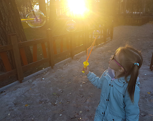 Image showing A little girl blowing soap bubbles in summer park. Background toninf for instagram filter