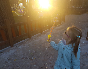 Image showing A little girl blowing soap bubbles in summer park.