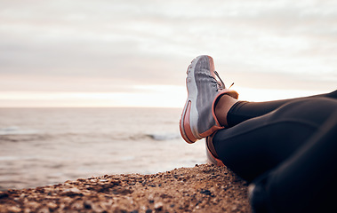 Image showing Fitness, shoes and sea in nature relax with freedom outdoor sitting. Waves, ocean and water with a person and athlete taking a break from training and workout with feet in sunset with mockup space