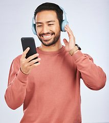 Image showing Man, headphones and smartphone for music in studio, white background and podcast app. Happy asian male model, cellphone and listening to audio, streaming mobile sound and online radio media with tech