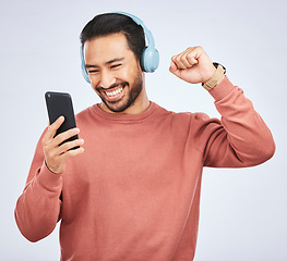 Image showing Man, headphones and celebrate success with smartphone, music and white background in studio. Asian male model, cellphone and fist for happy dance, excited audio deal and hearing winning news on radio