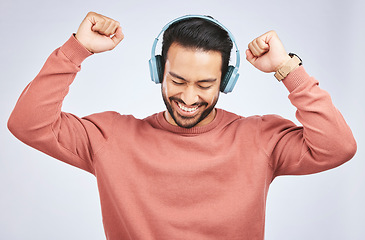 Image showing Man, headphones and dance to music in studio, white background and celebrate with energy. Happy, excited and young asian male model listening to audio, streaming sound and hearing rave song on radio