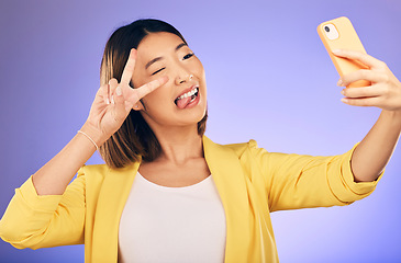 Image showing Asian woman, peace sign and funny face for selfie, photo or memory against a purple studio background. Happy female person or model pose with peaceful emoji, goofy or silly for picture or online vlog