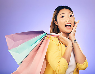 Image showing Asian woman, surprise and shopping bag with retail and fashion, commercial and sale on purple background. Wow for discount at boutique, happy female customer and market with store promotion in studio