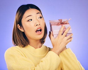 Image showing Surprise, gift and box with face of asian woman in studio for birthday, celebration and curious. Thinking, wow and party with female person and present on purple background for giveaway and package