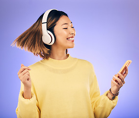Image showing Headphones, music and Asian woman dance with phone in studio for streaming, subscription and radio. Happy female person on smartphone listening to audio, song and track on purple background to relax