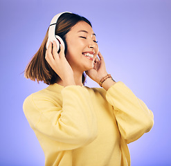 Image showing Headphones, dance and happy Asian woman with music in studio for streaming app, subscription and radio. Excited, podcast and female person listening to audio, song and track on purple background