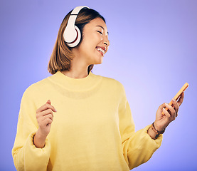 Image showing Music, phone and happy Asian woman in studio for social media, internet meme and online chat. Headphones, smile and female person on smartphone listening to audio, song and track on purple background