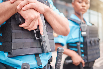 Image showing Police, hand and gun with a law enforcement officer standing outdoor in the city while on patrol closeup. Security, safety and protection detail with a guard on the street for crime prevention