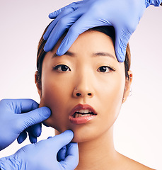 Image showing Asian woman, surgery and pinch facial skin in studio for cosmetic, inspection and hands in gloves by white background. Beauty, doctors and check for patient, transformation or shock for pain on face