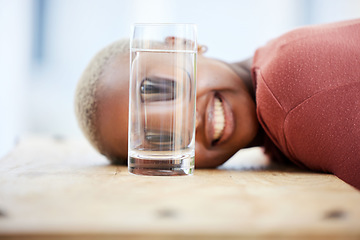 Image showing Woman, funny face and water glass with big eyes, laughing and comic joke on table in apartment. African girl, crazy young student and comedy for meme with happy smile, home and playing game on desk