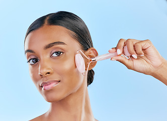 Image showing Face, massage and woman with roller, beauty and skincare, natural cosmetics and tools isolated on blue background. Rose quartz, crystal and skin glow, Indian female model in portrait with dermatology