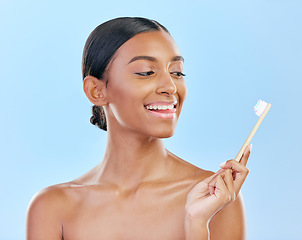 Image showing Face, toothbrush and a woman brushing teeth for dental health on a blue background for wellness. Happy indian female model with toothpaste and brush for a clean, fresh and healthy mouth in studio