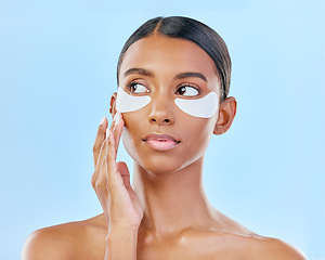 Image showing Face, eye patch and beauty of a woman with natural skin glow on a blue background. Dermatology, collagen mask and cosmetics of Indian female model for facial shine, wellness or self care in studio