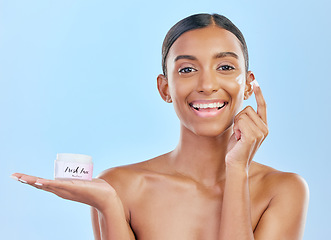 Image showing Face cream, skin and beauty portrait of a happy woman with natural glow on a blue background. Dermatology, moisturizer and cosmetics of Indian female model with a product container on hand in studio