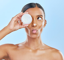 Image showing Woman, face and cream jar in studio, blue background and cosmetics with kiss emoji. Indian female model, facial expression and beauty lotion in container for glow, skincare results and makeup product